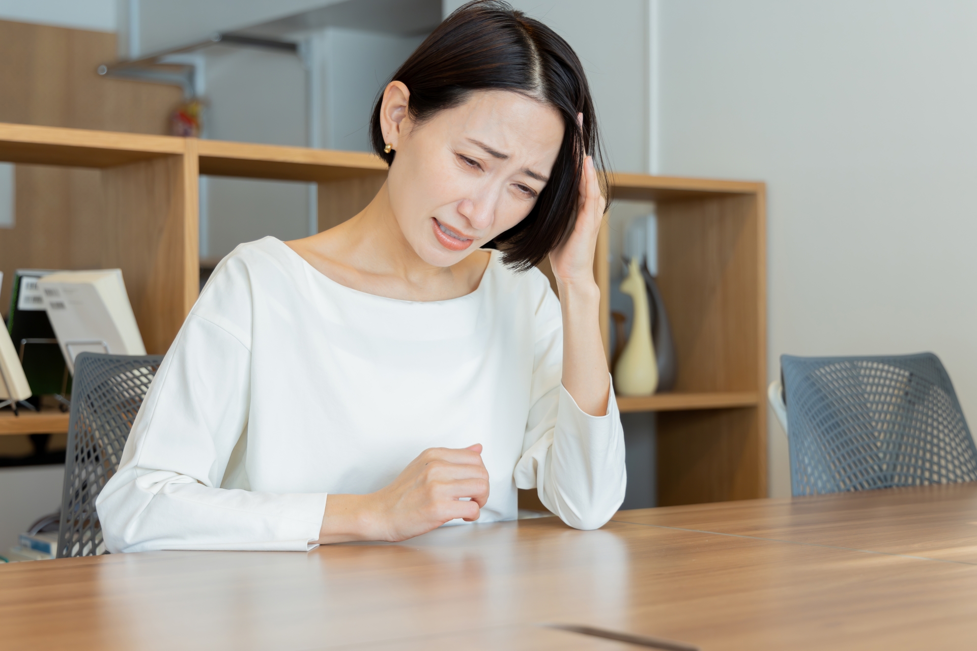 テーブルで頭を押さえてストレスを感じる女性