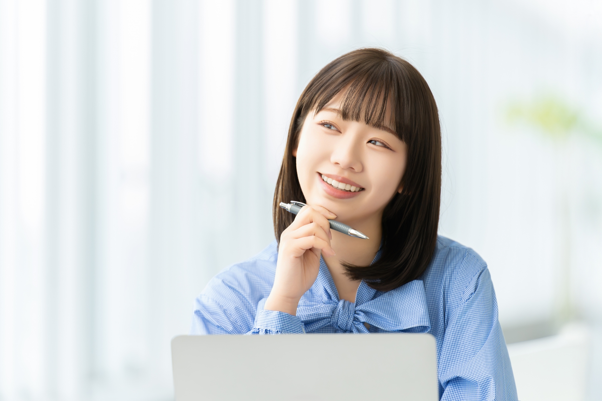 ペンを持ちながら笑顔で考える女性